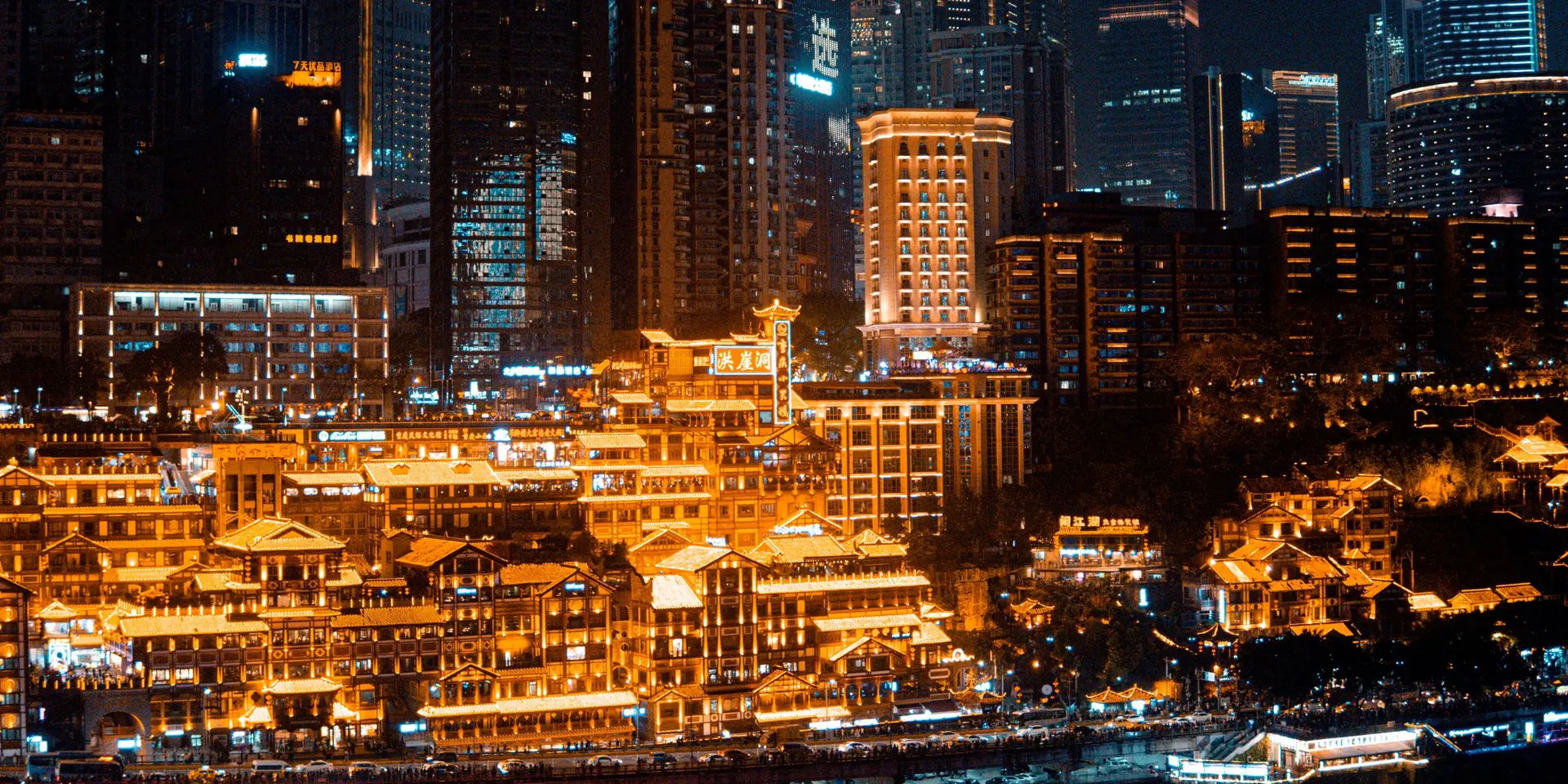 Hongyadong (洪崖洞) in Chongqing lit gold at night, stilted riverside buildings below the illuminated towers of Yuzhong